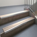 Mill Finish aluminium stair nosing fitted along two concrete steps in an office stairwell, with twin Sahara anti-slip inserts running the full width of each step