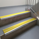 Mill Finish aluminium stair nosing fitted along two concrete steps in an office stairwell, with twin Yellow anti-slip inserts running the full width of each step