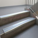 Mirroflect Silver aluminium stair nosing fitted along two concrete steps in an office stairwell, with twin Aura anti-slip inserts running the full width of each step