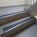 Mirroflect Silver aluminium stair nosing fitted along two concrete steps in an office stairwell, with twin Blue anti-slip inserts running the full width of each step