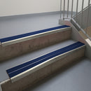 Mirroflect Silver aluminium stair nosing fitted along two concrete steps in an office stairwell, with twin Dark Blue anti-slip inserts running the full width of each step