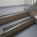 Mirroflect Silver aluminium stair nosing fitted along two concrete steps in an office stairwell, with twin Dark Grey anti-slip inserts running the full width of each step