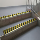 Mirroflect Silver aluminium stair nosing fitted along two concrete steps in an office stairwell, with twin Hazard black and yellow anti-slip inserts running the full width of each step