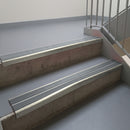 Mirroflect Silver aluminium stair nosing fitted along two concrete steps in an office stairwell, with twin Mid Grey anti-slip inserts running the full width of each step