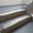 Mirroflect Silver aluminium stair nosing fitted along two concrete steps in an office stairwell, with twin Oyster anti-slip inserts running the full width of each step