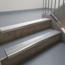 Mirroflect Silver aluminium stair nosing fitted along two concrete steps in an office stairwell, with twin Polar Grey anti-slip inserts running the full width of each step