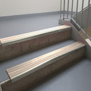 Mirroflect Silver aluminium stair nosing fitted along two concrete steps in an office stairwell, with twin Sahara anti-slip inserts running the full width of each step