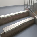 Mirroflect Silver aluminium stair nosing fitted along two concrete steps in an office stairwell, with twin White anti-slip inserts running the full width of each step