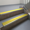 Mirroflect Silver aluminium stair nosing fitted along two concrete steps in an office stairwell, with twin Yellow anti-slip inserts running the full width of each step