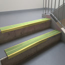 Mirrorflect Gold aluminium stair nosing fitted along two concrete steps in an office stairwell, with twin Apple Green anti-slip inserts running the full width of each step