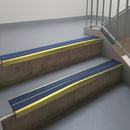 Mirrorflect Gold aluminium stair nosing fitted along two concrete steps in an office stairwell, with twin Blue anti-slip inserts running the full width of each step
