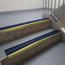 Mirrorflect Gold aluminium stair nosing fitted along two concrete steps in an office stairwell, with twin Dark Blue anti-slip inserts running the full width of each step