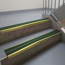 Mirrorflect Gold aluminium stair nosing fitted along two concrete steps in an office stairwell, with twin Dark Green anti-slip inserts running the full width of each step