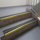 Mirrorflect Gold aluminium stair nosing fitted along two concrete steps in an office stairwell, with twin Dark Grey anti-slip inserts running the full width of each step