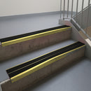 Mirrorflect Gold aluminium stair nosing fitted along two concrete steps in an office stairwell, with twin Premium Black anti-slip inserts running the full width of each step