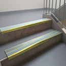 Mirrorflect Gold aluminium stair nosing fitted along two concrete steps in an office stairwell, with twin Sage Green anti-slip inserts running the full width of each step