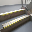 Mirrorflect Gold aluminium stair nosing fitted along two concrete steps in an office stairwell, with twin White anti-slip inserts running the full width of each step