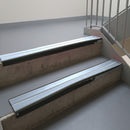 Satin Black aluminium stair nosing fitted along two concrete steps in an office stairwell, with twin Aura anti-slip inserts running the full width of each step