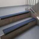 Satin Black aluminium stair nosing fitted along two concrete steps in an office stairwell, with twin Blue anti-slip inserts running the full width of each step