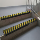 Satin Black aluminium stair nosing fitted along two concrete steps in an office stairwell, with twin Hazard black and yellow anti-slip inserts running the full width of each step