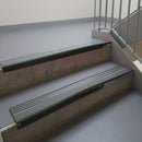 Satin Black aluminium stair nosing fitted along two concrete steps in an office stairwell, with twin Mid Grey anti-slip inserts running the full width of each step