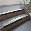 Satin Black aluminium stair nosing fitted along two concrete steps in an office stairwell, with twin Oyster anti-slip inserts running the full width of each step