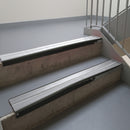 Satin Black aluminium stair nosing fitted along two concrete steps in an office stairwell, with twin Polar Grey anti-slip inserts running the full width of each step