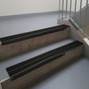 Satin Black aluminium stair nosing fitted along two concrete steps in an office stairwell, with twin Premium Black anti-slip inserts running the full width of each step