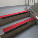Satin Black aluminium stair nosing fitted along two concrete steps in an office stairwell, with twin Red anti-slip inserts running the full width of each step