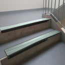 Satin Black aluminium stair nosing fitted along two concrete steps in an office stairwell, with twin Sage Green anti-slip inserts running the full width of each step