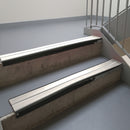 Satin Black aluminium stair nosing fitted along two concrete steps in an office stairwell, with twin White anti-slip inserts running the full width of each step