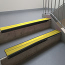 Satin Black aluminium stair nosing fitted along two concrete steps in an office stairwell, with twin Yellow anti-slip inserts running the full width of each step