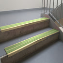 Satin Bronze aluminium stair nosing fitted along two concrete steps in an office stairwell, with twin Apple Green anti-slip inserts running the full width of each step