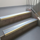 Satin Bronze aluminium stair nosing fitted along two concrete steps in an office stairwell, with twin Aura anti-slip inserts running the full width of each step