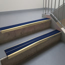 Satin Bronze aluminium stair nosing fitted along two concrete steps in an office stairwell, with twin Dark Blue anti-slip inserts running the full width of each step