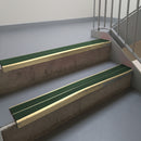 Satin Bronze aluminium stair nosing fitted along two concrete steps in an office stairwell, with twin Dark Green anti-slip inserts running the full width of each step