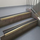 Satin Bronze aluminium stair nosing fitted along two concrete steps in an office stairwell, with twin Dark Grey anti-slip inserts running the full width of each step