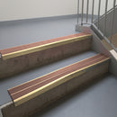 Satin Bronze aluminium stair nosing fitted along two concrete steps in an office stairwell, with twin Mid Brown anti-slip inserts running the full width of each step