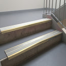 Satin Bronze aluminium stair nosing fitted along two concrete steps in an office stairwell, with twin Oyster anti-slip inserts running the full width of each step