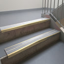 Satin Bronze aluminium stair nosing fitted along two concrete steps in an office stairwell, with twin Polar Grey anti-slip inserts running the full width of each step