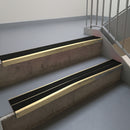 Satin Bronze aluminium stair nosing fitted along two concrete steps in an office stairwell, with twin Premium Black anti-slip inserts running the full width of each step