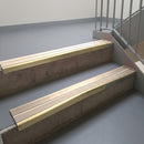 Satin Bronze aluminium stair nosing fitted along two concrete steps in an office stairwell, with twin Sahara anti-slip inserts running the full width of each step