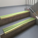 Satin Gold aluminium stair nosing fitted along two concrete steps in an office stairwell, with twin Apple Green anti-slip inserts running the full width of each step