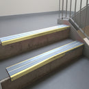 Satin Gold aluminium stair nosing fitted along two concrete steps in an office stairwell, with twin Aura anti-slip inserts running the full width of each step