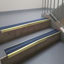 Satin Gold aluminium stair nosing fitted along two concrete steps in an office stairwell, with twin Blue anti-slip inserts running the full width of each step