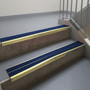 Satin Gold aluminium stair nosing fitted along two concrete steps in an office stairwell, with twin Dark Blue anti-slip inserts running the full width of each step