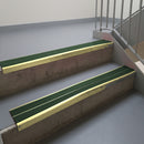 Satin Gold aluminium stair nosing fitted along two concrete steps in an office stairwell, with twin Dark Green anti-slip inserts running the full width of each step