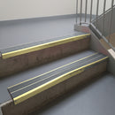 Satin Gold aluminium stair nosing fitted along two concrete steps in an office stairwell, with twin Mid Grey anti-slip inserts running the full width of each step