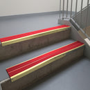 Satin Gold aluminium stair nosing fitted along two concrete steps in an office stairwell, with twin Red anti-slip inserts running the full width of each step