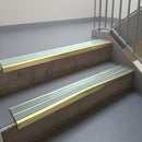 Satin Gold aluminium stair nosing fitted along two concrete steps in an office stairwell, with twin Sage Green anti-slip inserts running the full width of each step